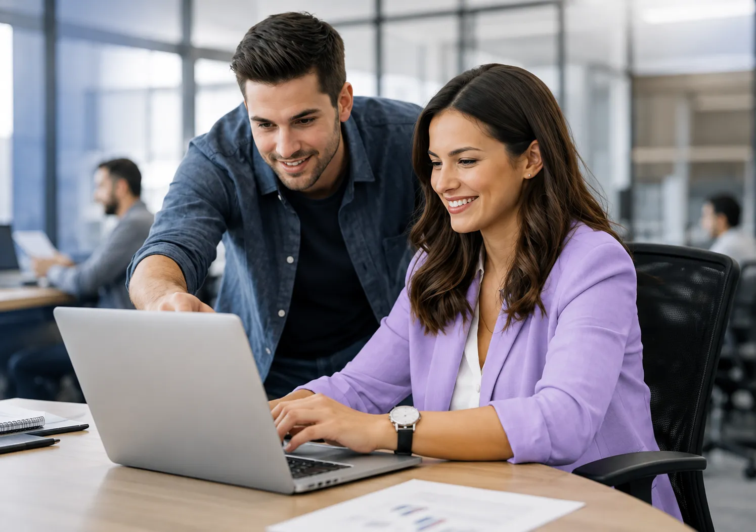 Two colleagues reviewing an operations dashboard on a laptop in an open-plan office