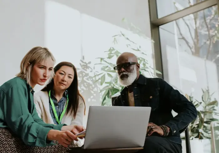 A mentor working through a problem with two colleagues at a laptop